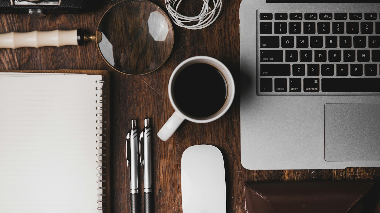 Tidy desk with laptop, coffee cup, notebook and pens