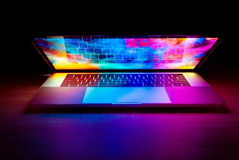 Laptop with a glowing colorful screen on a dark wooden desk
