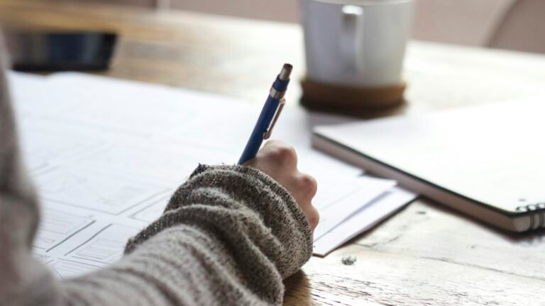Person writing notes at a desk next to a coffee mug